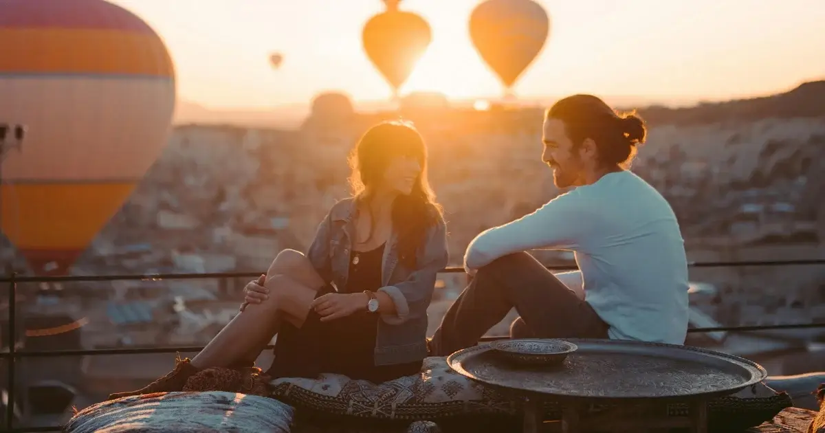 A couple sitting infront of hot air balloons and beautiful sunset.