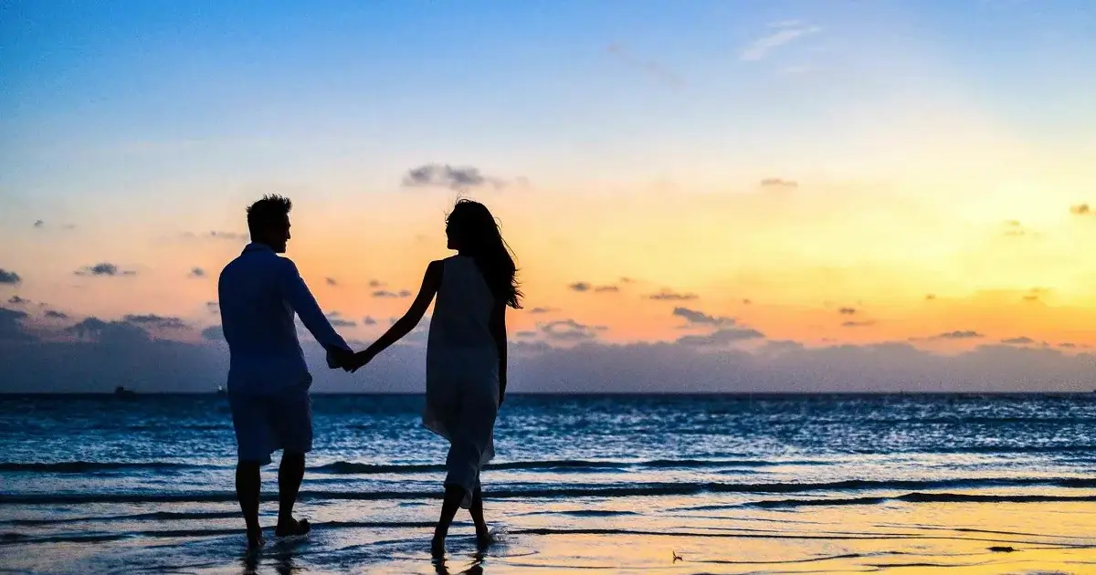 A couple on a sandy beach with a beautiful sunset. Holding hands.