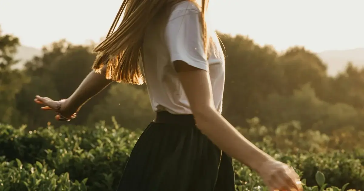 A woman walking away in tall grass and sunset