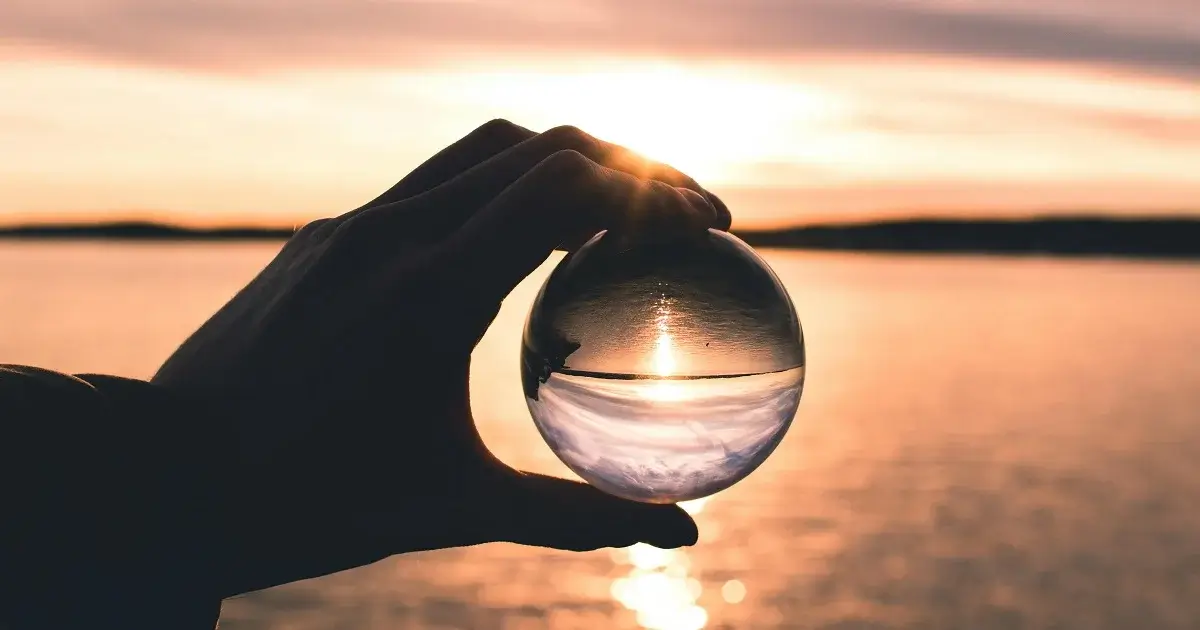 A ball made of glass being held up infront of a sunset, reflecting a different perspective of the world.