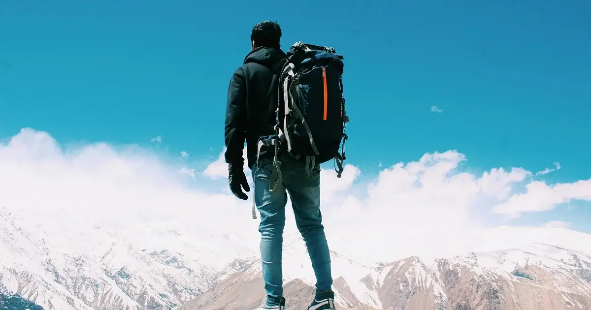 Man hiking in the mountains with snow on the mountaintops.